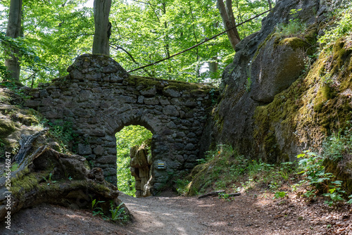 Bild auf Leinwand Ancient medieval stone arch gateway of ruined castle surrounded by lush green forest and mossy rocks on a sunny summer day