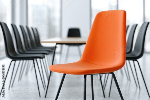 Modern corporate meeting room featuring an orange chair in the foreground with black chairs arranged around a wooden table and large windows providing natural light