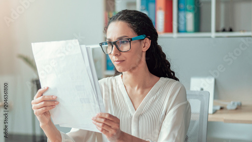Quadro su tela Concerned African American Woman In Her 30s Examining Important Documents At Her Desk In Modern Office Setting, Concentrating On Details And Information