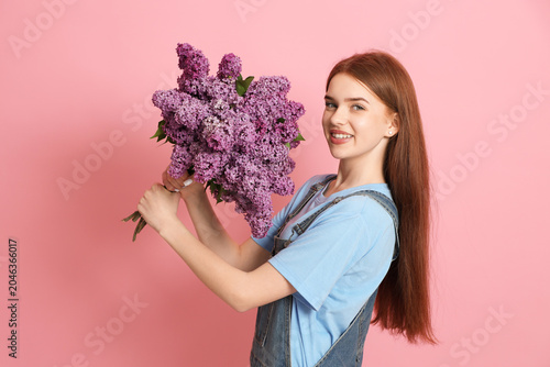 Teenage girl with bouquet of lilac flowers on pink background