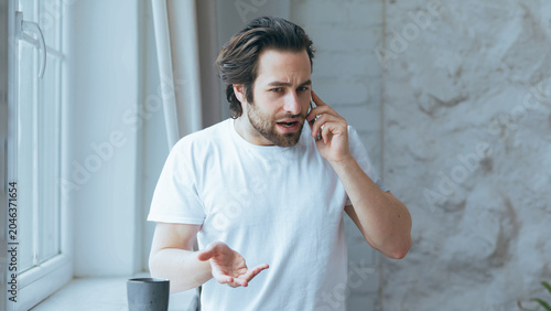 Photos Worried Man, Caucasian, Adult, Engaged In Phone Conversation At Home, Showing Concerned Expression While Standing By Window