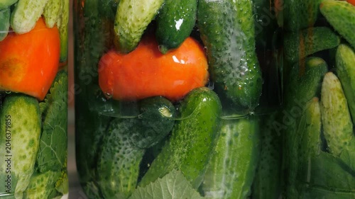 Home preservation. Assorted tomatoes with cucumbers in glass jars are poured with boiling water.