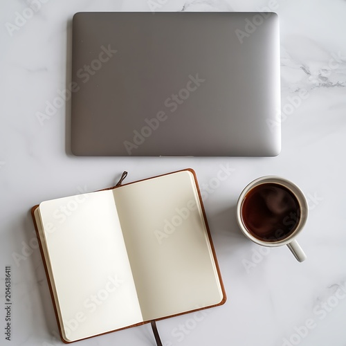 Overhead view of an open blank notebook next to a steaming cup of dark coffee and a closed silver laptop on a white marble surface work study or creative planning Keywords: work, study, coffee