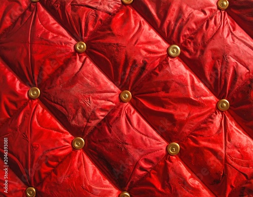 Close-up of richly textured red fabric with a diamond-pattern and gold buttons, suggesting luxury and elegance