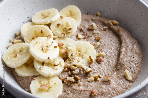Healthy flaxseed porridge topped with banana slices, chopped nuts and seeds in a ceramic bowl. Nutritious breakfast with natural ingredients, close up view
