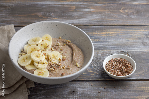 Healthy flaxseed porridge topped with banana slices, chopped nuts and seeds in a ceramic bowl. Nutritious breakfast with natural ingredients, copy space