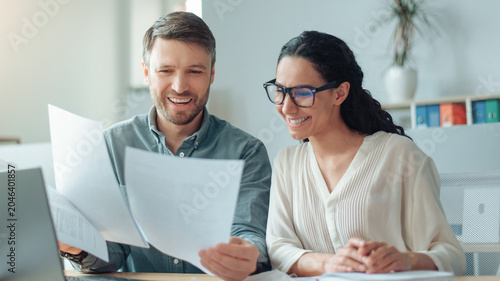 Tableau sur toile Smiling Caucasian Man And Woman Analyzing Documents And Discussing Ideas In A Bright Modern Office, Collaborating And Sharing Insights As Part Of Their Professional Work Environment