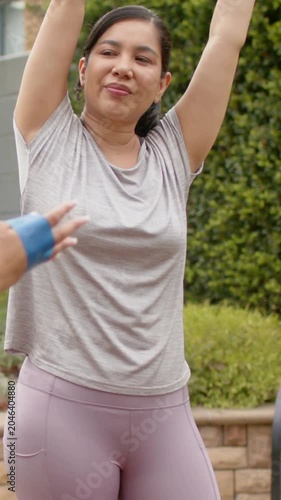 Vertical video: Warming up woman taking grey band and pulling overhead on patio in grey top