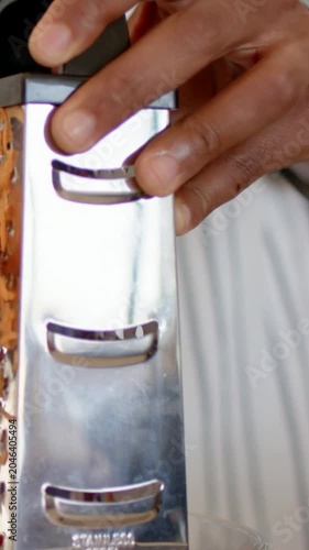 Vertical video: Grating man holding grater, pressing carrot making shreds in kitchen with bracelet