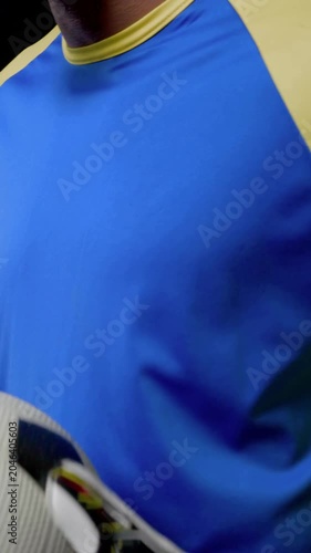 Vertical video: Holding ball, gloved keeper in blue-yellow kit adjusting grip, pushing ball right