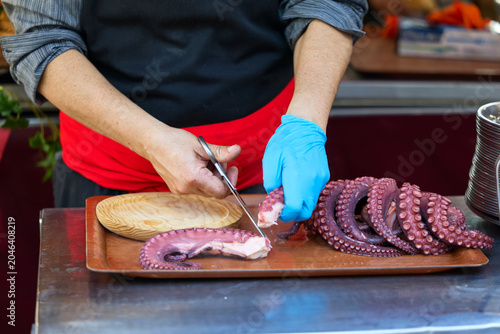 Gloved hands cutting octopus on a board