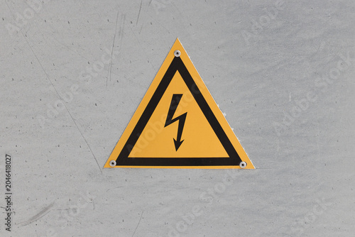 Yellow danger electricity warning sign on a grey industrial background