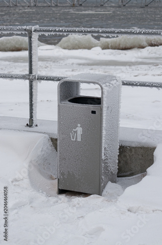 Frozen trash bin on a snowy waterfront in winter