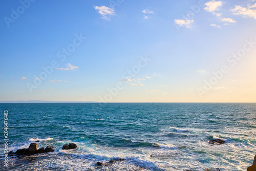 Bild auf Leinwand Serene ocean horizon at sunset with rocky shoreline and clear blue sky