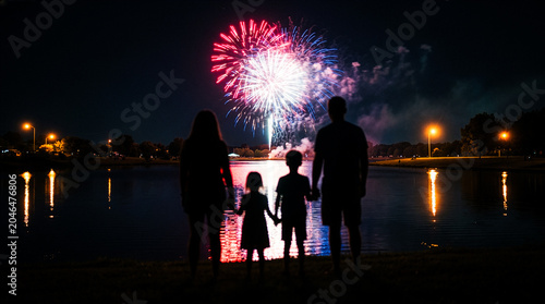 фотографія Family silhouetted watching colorful fireworks display over lake at night with r