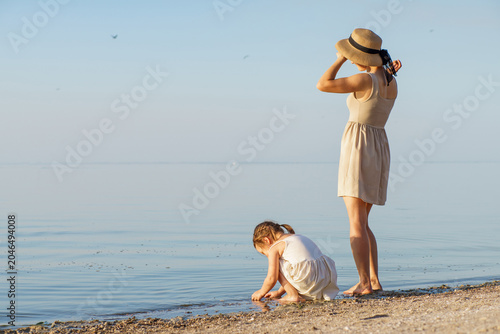 A happy childhood. A mother and daughter stroll along a sandy beach by the lake. A mother and little girl relax on the beach.