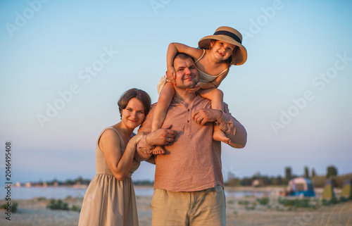 A happy family enjoys the beautiful sunset views. The father put his daughter on his neck.