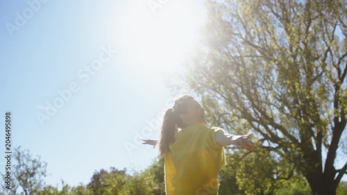 A woman in a yellow sweater spins with joy in a sun-drenched park, expressing freedom and happiness through movement during a beautiful spring day in nature.