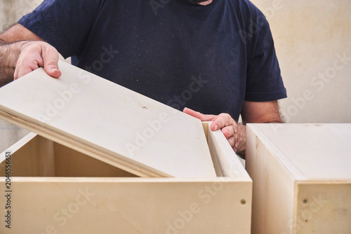 Fotografie Close-up of a wooden piece of furniture, showing a carpenter's hands as he attaches the final back panel