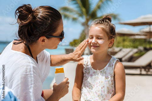 Mother applying sunscreen on daughters face.
