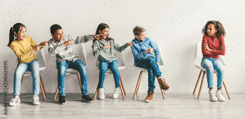 Photos Annoyed Girl Sitting Alone As Diverse Group Of Kids Point And Laugh At Her In Studio Setting