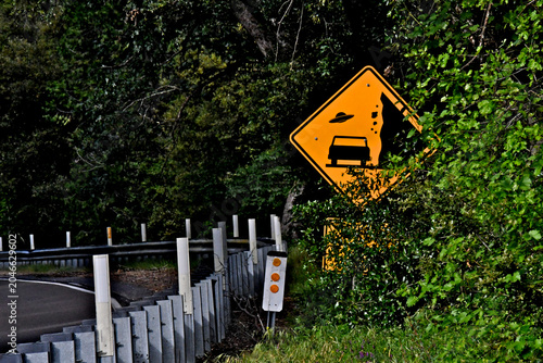 Yellow sign warning motorists of falling rocks and flying saucer up ahead, Sierra Nevada Foothills, California 