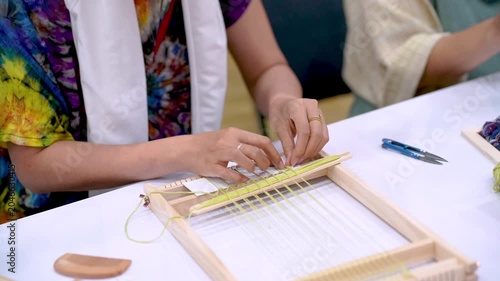 Hands Weaving Threads on Wooden Loom During Textile Workshop