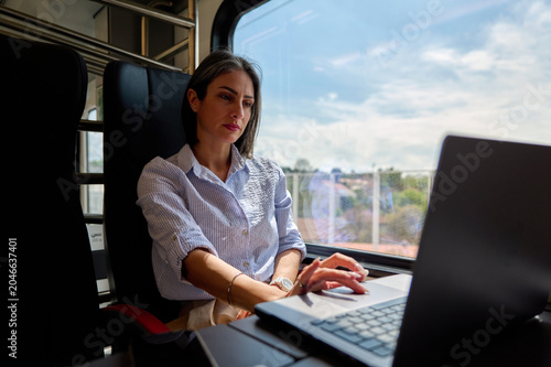 Woman focused on laptop in train window seat, working remotely during a business trip, digital nomad style productivity and connectivity on the go in a comfortable commuter setting
