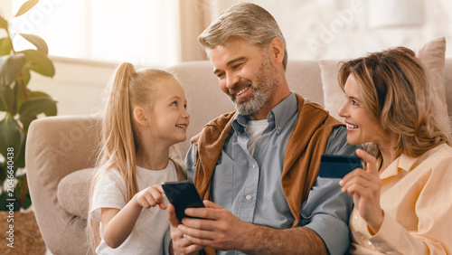 Foto Smiling Caucasian Grandfather, Father And Young Daughter Engaged With Smartphone At Home, Enjoying Family Time Together In Cozy Living Room, Strengthening Their Bond