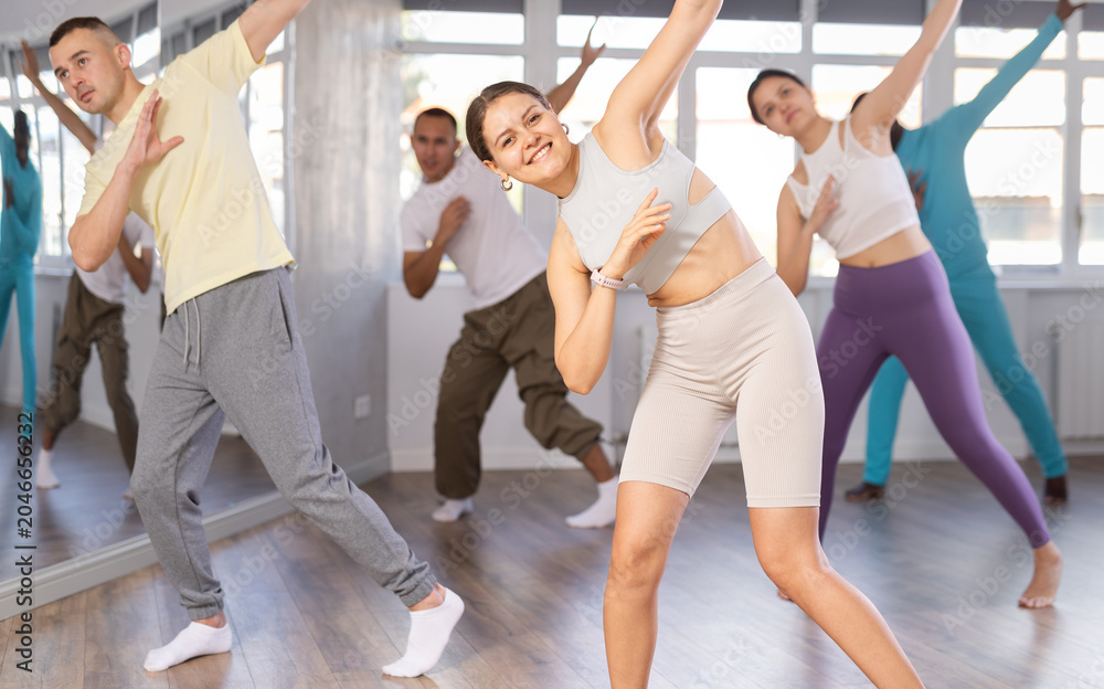 Fototapeta premium European girl teaches sequences of movements, actions during dance lesson, trains to doing elements of electro dance, enjoys active hobby. Multinational group rehearsal, dance choreography coach