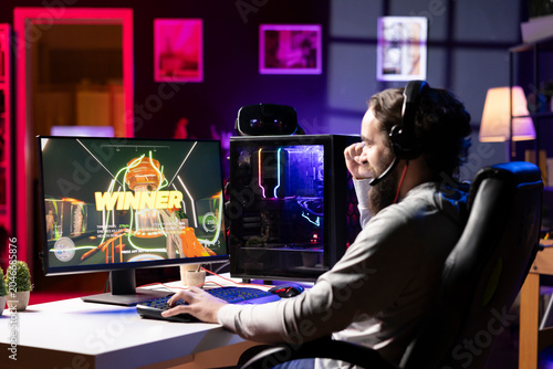 Canvas-taulu Gamer in neon lit apartment excited after winning level in first person shooter, killing all enemies