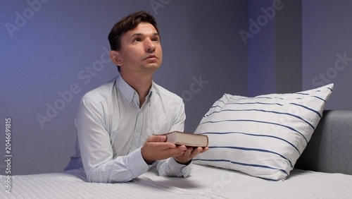Bild auf Leinwand Man kneeling on a bed, holding a bible and looking up in quiet evening prayer, a