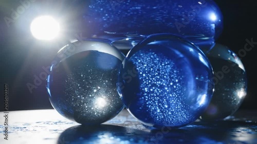 Blue glass spheres reflecting bright light on dark surface.