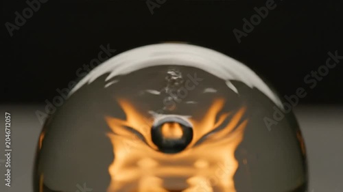 A glass orb reflects a burning fire in a dark room setting.