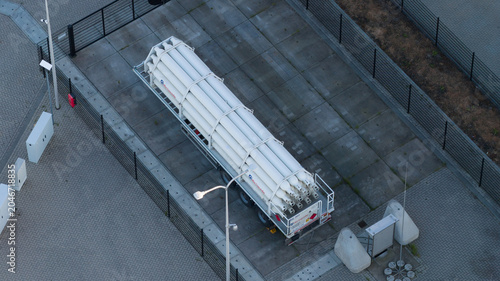 Roosendaal, Netherlands - 25 April 2026: Aerial view of a trailer loaded with white pressurized gas cylinders parked within a fenced industrial compound.