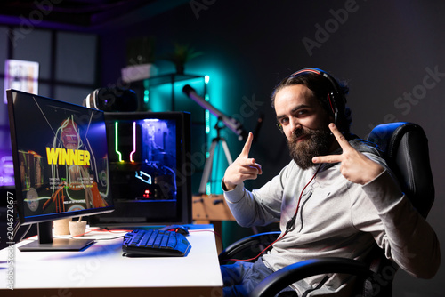 Obraz na plátne Jolly gamer in RGB lit home bragging after winning level in first person shooter, killing all enemies