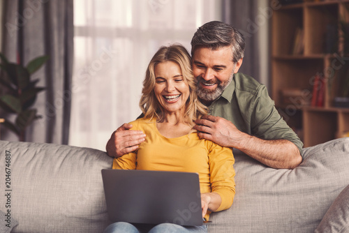 Fotografía Happy Caucasian, Middle-aged, Smiling Together While Using Laptop On Sofa At Home