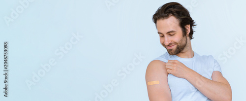 Tableau sur toile Smiling Young Caucasian Man With Bandage On Arm After Vaccination, Showing Emotion In Clinic, Taking Care Of Health