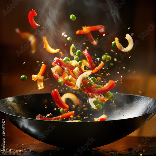 Vibrant wok stir-fry with fresh vegetables and spices flying in the air - concept of asian cuisine magic