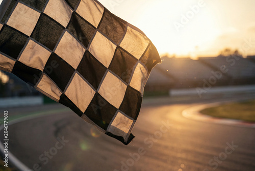 Black and white checkered racing flag waving at the finish line of a track during sunset