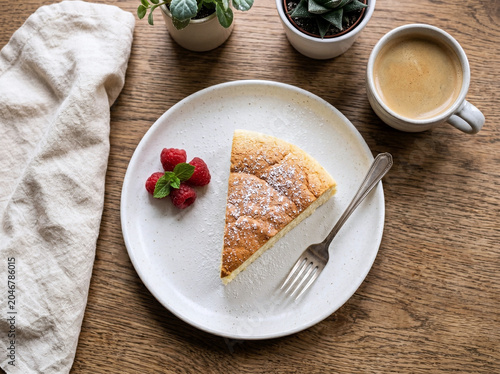 真上から見たウッドテーブルの上のスフレチーズケーキとラズベリーとコーヒー