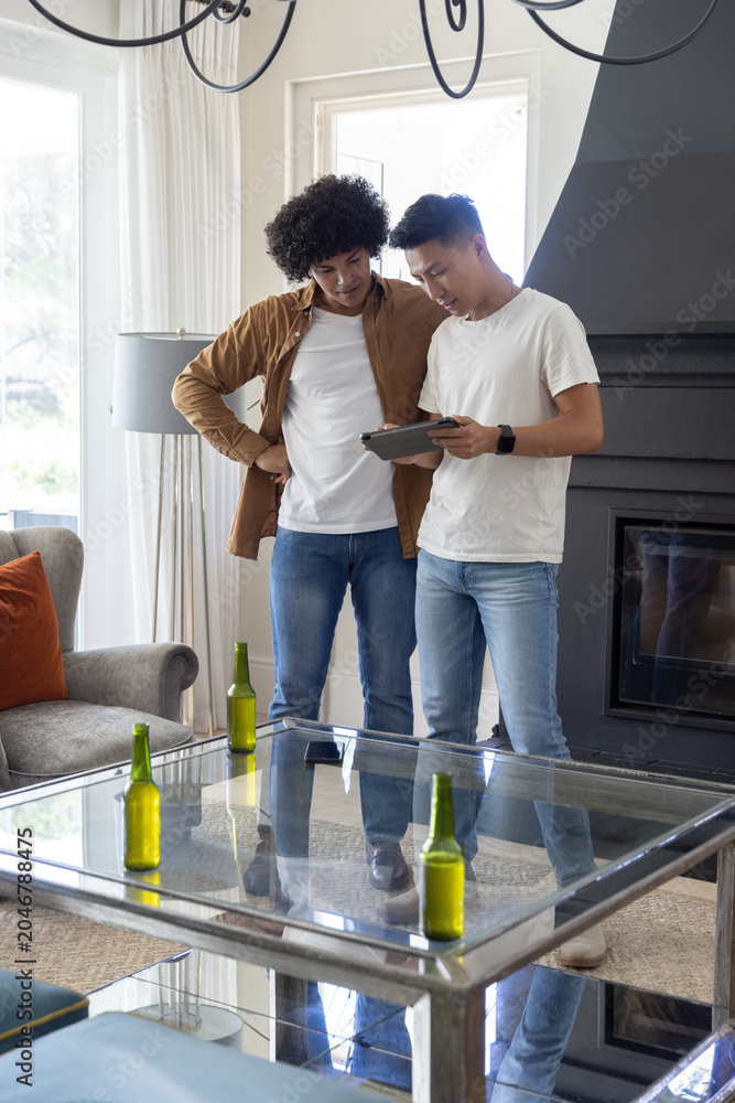 Obraz premium Diverse male friends leaning in, examining tablet while standing in living room with green bottles