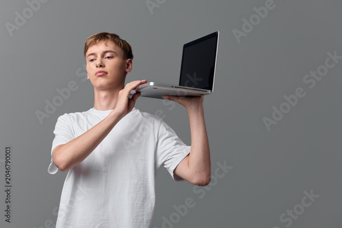Cuadro en lienzo Laptop held aloft by casual youth against a neutral backdrop, emphasizing techno