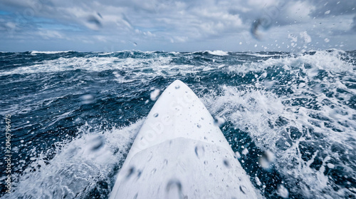 POV from a windsurfer board slicing through choppy deep blue ocean water with sea spray