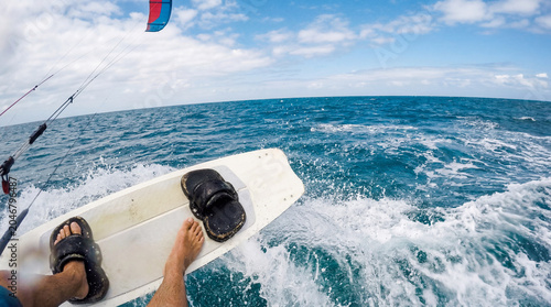 Wide angle POV from kiteboarding deck flying over a small cresting ocean wave with spray