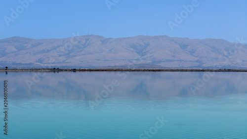 A tranquil view of the Diablo Range in Alameda County, California, rising beyond the still waters of a bay or wetland, as seen from Sunnyvale Bay Trail.