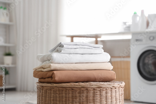 Stack of clean bed sheets on basket in laundry room
