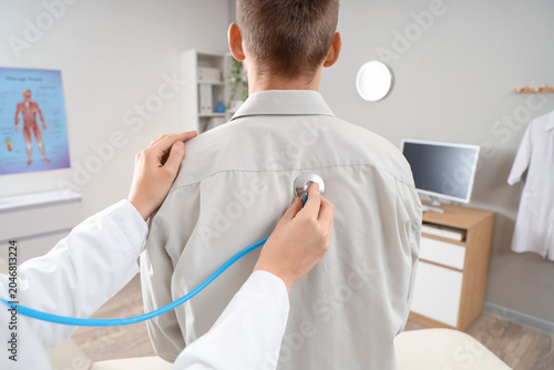 Female doctor with stethoscope listening to male patient at hospital, back view