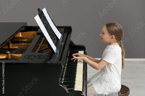 Cute little happy girl with notes playing grand piano at home