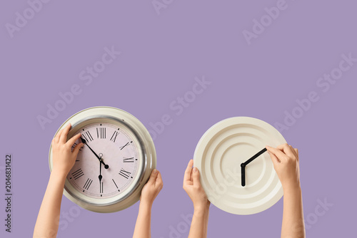 Bild auf Leinwand Female hands holding different wall clocks on lilac background